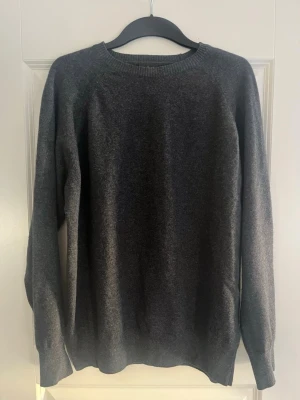 Mörkgrå stickad tröja OscarJacobsson - Mörkgrå stickad tröja från OJ med rund halsringning och långa ärmar. Tröjan har en diskret OJ-logga nere i hörnet på tröjan. Skicket är nästintill oanvänd 