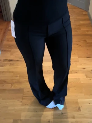 Svarta utsvängda kostymbyxor - Snygga svarta kostymbyxor med utsvängda ben och låg midja. Byxorna har pressveck framtill och stängs med dragkedja och knapp. Perfekta för en stilren look och passar till många olika outfits. Helt nya, prislapp kvar då de endast är testade. Stl 38 på lapp men definitivt stl 36 i passform