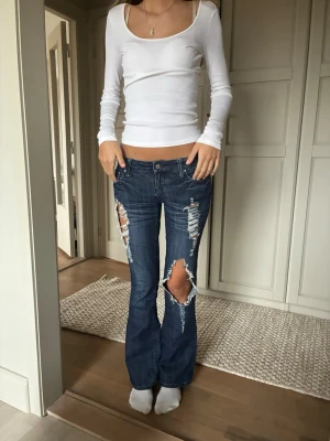 Mörkblå slitna bootcut jeans - Säljer mina jättesnygga mörkblå bootcut jeans med hål. Jeansen har låg midja och klassiska femficksdetaljer. Det står tyvärr ingen storlek men skriv till mig för mått osv! Jag är öppen för prisförslag💕💕
