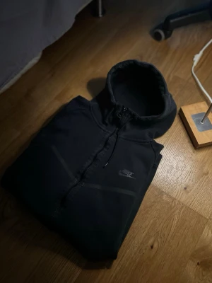 Svart Nike hoodie med dragkedja - Säljer en svart hoodie från Nike med dragkedja och huva. Hoodien har diskret Nike-logga på bröstet och är tillverkad i mjukt material.Den är L men är en M.