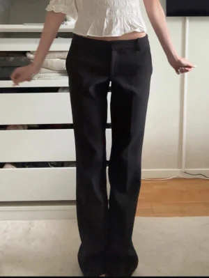 Svarta lågmidjade kostymbyxor  - Säljer ett par svarta kostymbyxor från Bikbok med raka ben och en låg midja. Byxorna har bälteshällor, sidofickor och stängs med knapp och dragkedja. Stl 34, passar mig bra i längden som är 1,65 med långa ben. Lite noppriga annars i fint skick💕modellen Vera!!