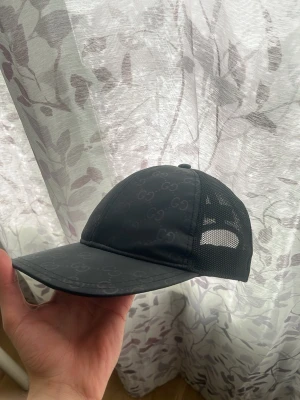 Svart keps från Gucci med mesh - Snygg svart keps från Gucci med diskret GG-mönster över hela kepsen. Kepsen har böjd skärm och sidor i mesh för extra ventilation. Perfekt accessoar för en trendig streetwear-look.