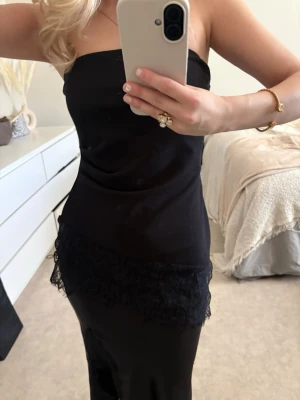 Svart axelbandslös topp - Säljer en svart axelbandslös topp med spetsdetaljer nedtill. Toppen är elegant. Perfekt för dig som vill ha en stilren och klassisk look.