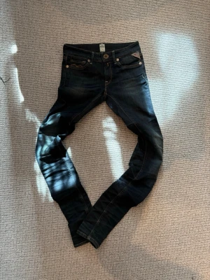 Mörkblå skinny jeans från Replay - Snygga mörkblå skinny jeans från Replay med klassiska fem fickor och bruna sömmar. Jeansen har smal passform hela vägen ner. Perfekta för dig som gillar en tight och modern look. Med slitningar som ger dig en avslappnad look.