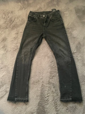 Svarta flared jeans från Zara - Snygga svarta jeans från Zara med rak passform och klassisk femficksdesign. Jeansen har en lätt tvättad look och råa kanter vid bensluten för en trendig touch. Perfekta för dig som gillar en stilren och avslappnad vibe.