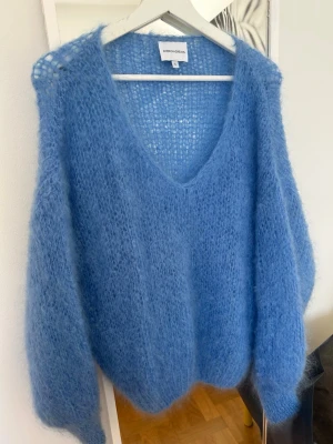 Blå fluffig stickad tröja American Dreams - Supersnygg blå stickad tröja från American Dreams med fluffig och luftig känsla. Tröjan har v-ringning, lång ärm och oversized passform. Perfekt för dig som gillar en mysig och trendig look. 78% mohair.