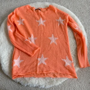 Persikofärgad stickad tröja med stjärnor - Superfin persikofärgad stickad tröja från Gina Tricot med vita stjärnor över hela tröjan. Tröjan har rund halsringning och långa ärmar. Perfekt för dig som vill ha en mysig och trendig look med lite extra färg.