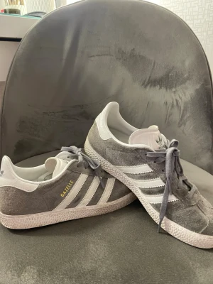 Adidas Gazelle grå sneakers - Snygga Adidas Gazelle sneakers i grå mocka med vita detaljer. De är i använt skick💗Storlek 36 1/2 men är mer som 37 1/2, jag har vanligtvis 38 och de är endast lite trånga💗