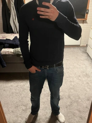Mörkblå stickad tröja med röd logga - Snygg mörkblå stickad tröja med en liten röd broderad logga på bröstet. Passar till både jeans och chinos. Skriv vid frågor, jag svarar snabbt!