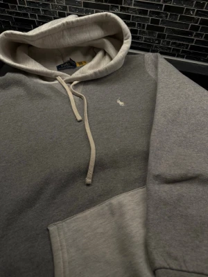 Polo Ralph Lauren hoodie  - Snygg och mycket unik grå hoodie från Polo Ralph Lauren med klassisk huva och dragsnören. Materialet är mjukt och bekvämt, perfekt för en avslappnad stil. Färgkombinationen går i ljusgrått och mörkgrått.
