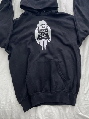 Svart hoodie med tryck från Fruit of the Loom - Cool svart hoodie från Fruit of the Loom i storlek XL. Tryck med Banksy-inspirerad apa och texten 'Laugh now, but one day we'll be in charge' på bröstet. Klassisk känguruficka och huva. Materialet är mjukt och bekvämt, perfekt för chill dagar. Hör av dig vid frågor😄