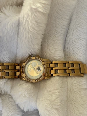 Klocka - Snygg guldig klocka från Dyrberg/kern med metallarmband och glittrande stenar runt urtavlan. Urtavlan har en unik design med romerska siffror och dekorativa detaljer. Perfekt accessoar för dig som gillar lite extra bling. (Funkar ej) men det går att fixa🤍