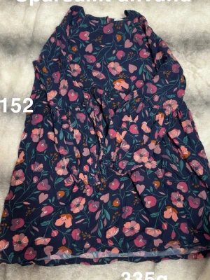 Blommig marinblå klänning med lång ärm - Söt marinblå klänning med blommigt mönster. Klänningen har lång ärm och resår i midjan för en bekväm passform. Perfekt för dig som gillar färgglada och lekfulla plagg.🌸Sparsamt använd. Storlek 152 