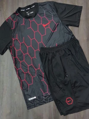 Svart Nike träningsset med rött mönster - Säljer ett svart träningsset från Nike med t-shirt och shorts. T-shirten har ett rött hexagonmönster och Nike-logga på bröstet, medan shortsen har en liten röd hexagon och logga. Setet är gjort i ett lätt och snabbtorkande material, perfekt för träning.