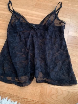 Svart spetslinnetopp med rosett - Snygg svart linnetopp i transparent spets med tunna axelband och liten rosett framtill. Toppen har ett spetsmönster med typ massa kvinnor(se sista bild) jätte fint skick, använd cirka 2 ggr. Vet ej storlek men tror den passar en xs till en liten m 