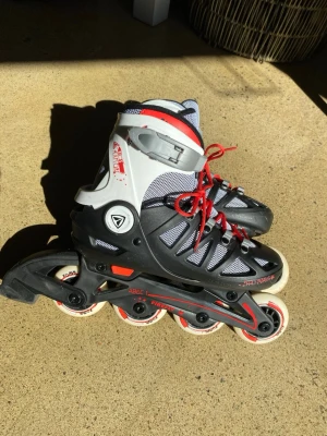 Firefly inlines med röda detaljer - Säljer ett par snygga inlines i svart och grått med röda snören och detaljer i storlek 33-36. De har ventilerande meshpartier och justerbart spänne upptill. Hjul i vitt med röda och svarta tryck. Perfekta för dig som vill cruisa runt i stan eller i parken.