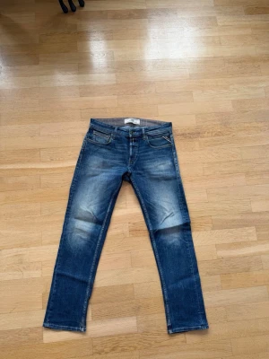 Blå slim fit jeans från Replay - Snygga blå slim fit jeans från Replay med slitningar och tvättade detaljer. Klassisk femficksmodell med dragkedja och knapp. Perfekta för en avslappnad och trendig look.