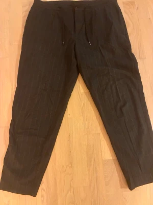 Svarta randiga mjukisbyxor med snörning - Snygga svarta mjukisbyxor med tunna vita ränder och snörning i midjan. Byxorna har en relaxed fit och är perfekta för en chill och avslappnad stil. Passar dig som gillar streetwear och vill ha något bekvämt men ändå stilrent.