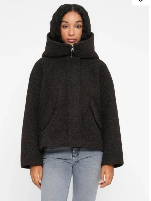 Mörkbrun jacka med hög krage - Mysig mörkbrun jacka med hög krage och dragkedja framtill. Jackan har två snedställda fickor och är tillverkad i ett ull-liknande material som ger en fluffig och varm känsla. Passformen är boxy med vida ärmar och kortare längd. Helt ny