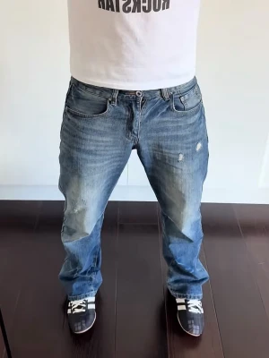Ljus blå bootcut / straight legg jeans - Säljer ett par blå jeans med raka ben och slitna detaljer på låren och knäna. Jeansen har klassisk femficksdesign och en avslappnad passform. Perfekta för en casual och trendig look.
