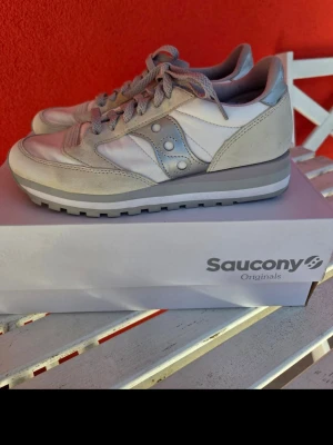 Saucony Originals vita sneakers - Snygga vita och ljusgrå sneakers från Saucony Originals. Skorna har klassisk retrodesign med mockadetaljer, meshpaneler och Sauconys ikoniska logga på sidan. Tjock sula för extra komfort och cool look. Perfekta för dig som gillar stilrena och tidlösa sneakers.