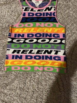 Färgglad mönstrad linnetopp - Säljer en färgglad linnetopp från Art Class med tryckt textmönster i flera färger som rosa, grön, gul, lila, svart och vit. Toppen är ärmlös och har en croppad passform, perfekt för dig som gillar att sticka ut med din stil.