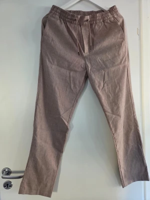 Beiga linnebyxor från H&M Slim Fit - Snygga beiga linnebyxor från H&M i modellen Slim Fit. Byxorna har resår och dragsko i midjan för skön passform samt raka ben. Perfekta för en avslappnad och stilren look. Tillverkade i ett lätt och luftigt linnematerial.