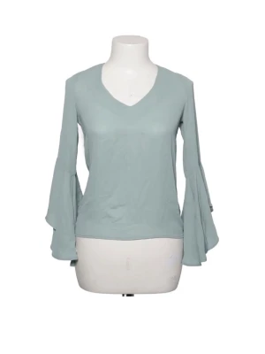 Mintgrön topp med trumpetärmar från NA-KD - Trendig mintgrön topp med v-ringning och vida trumpetärmar. Baksidan har en snygg öppen detalj med knytband i nacken. Tillverkad i ett mjukt, lätt material som känns skönt mot huden. Sparsamt använd.