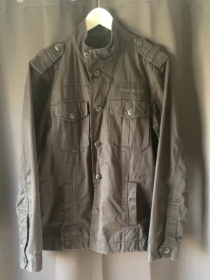 Fieldjacka  - Tjenaret! Säljer en svart Fieldjacka med fickor och snygga axelpartier. Jackan har två stora bröstfickor med knappar, ståkrage och dekorativa detaljer på axlarna. Materialet är slitstarkt och i någon form av jeans! Knappstängning hela vägen! Perfekt för dig som gillar en fet och helt enkelt stilren jacka! Storlek M, 8,5/10 skick= en knapp som lossnat som följer med! Hör av dig vid mer frågor eller funderingar🤩mvh premium fashion 