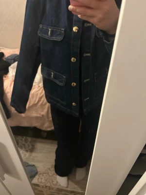Mörkblå jeansjacka med guldknappar - Snygg trendig mörkblå jeans jacka med fickor o gul knappar framtill! Är 165cm och den är liiite stor på mig därför kommer den inte till användning o har använt den en kväll!!🥰🥰