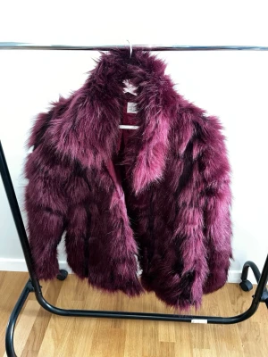 Vinröd fuskpälsjacka från NLY Trend - Vinröd fuskpälsjacka från NLY Trend med fluffig och voluminös look. Jackan har bred krage och är helfodrad i matchande vinröd färg. Perfekt statement-plagg för dig som vill sticka ut med en trendig och djärv stil. Har några små hål på insidan men inget som syns när den används. Storlek 34