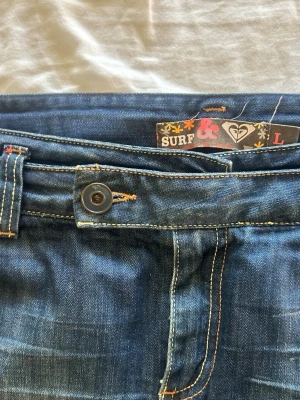 Vintage lowwaist jeanskjol Roxy - Säljer en mörkblå lågmidjad 2000s jeans kjol från Roxy med klassisk femficksdesign och knappgylf. Kjolen har en kort och rak passform med slitna detaljer och kontrastsömmar. Perfekt till sommaren för en avslappnad look. Strl L men skulle säga att den passar M lika väl!!