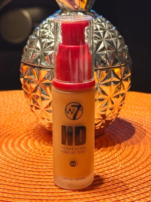 W7 HD Foundation Tan 30ml - W7 HD Foundation i nyansen Tan ger en jämn och naturlig finish. Kommer i en praktisk pumpflaska på 30 ml med röd plastkork. Perfekt för dig som vill ha en täckande bas med lång hållbarhet. Flytande formula som är lätt att applicera. Flaskan är öppnad och endast provad. 