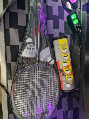 Badmintonset med racket och bollar - Badmintonset med två racketar i svart och rött, tre vita plastfjädrar och ett fodral. Medföljer även ett rör med flera badmintonbollar. Perfekt för spel utomhus eller i hallen.