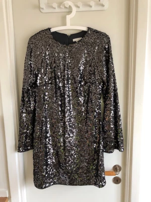 Glittrig silverklänning från H&M - Säljer en glittrig silverfärgad klänning från H&M, täckt med paljetter. Klänningen har lång ärm, rund halsringning och dragkedja i ryggen. Perfekt för dig som vill sticka ut och glänsa på nästa fest!