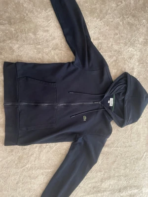 Lacoste zip up hoodie - Marinblå Lacoste zip up hoodie i storlek S. Köpte den för 1799kr 1 månad sedan från careofcarl.se och har knappt tagit på mig den