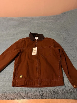 Brun jacka med kontrastkrage från Zara - Snygg brun jacka från Zara med svart kontrastkrage och dragkedja framtill. Jackan har en bröstficka, knappdetaljer vid ärmslut och en liten patch nertill. Perfekt för dig som gillar stilren och trendig design.