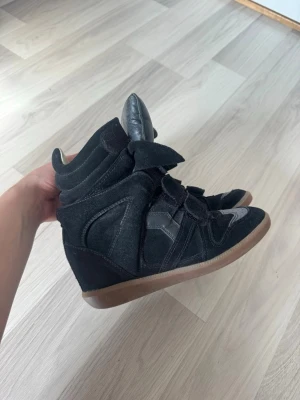 Svarta Isabel Marant wedge sneakers - Säljer ett par svarta Isabel Marant wedge sneakers med högt skaft och kardborreband. Älskar skorna men tyvärr inte kommit till användning så mycket som jag hoppats på. Storlek 35 men jag har vanligtvis storlek 36 och dem passar mig bra ändå, har man lite bredare fötter kanske dem inte gör det. 