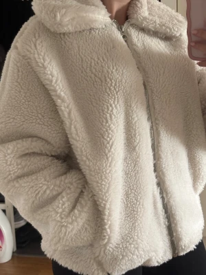 Vit teddyjacka från Weekday XS - Supermjuk och fluffig teddyjacka från Weekday i krämvit färg. Jackan har dragkedja framtill, hög krage och två sidofickor. Perfekt för dig som vill ha en mysig och trendig look. Materialet är fuskpäls i teddy-stil. oversized passform. Aldrig använd.