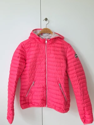 Rosa dunjacka med huva från Colmar - Snygg rosa dunjacka från Colmar med huva och dragkedja framtill. Jackan har två fickor med dragkedja och ett märke på ärmen. Lättviktig och quiltad design som håller dig varm under kalla dagar. Funkar året om. 