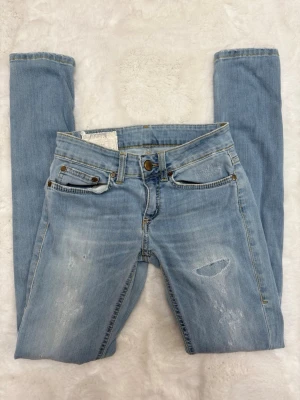 Dondup skinny | W27 - Säljer ett par ljusblå jeans från Dondup med slitna detaljer och klassisk femficksmodell. Jeansen har gylf med dragkedja och knapp, samt snygga kontrastsömmar och Dondup-logga på bakfickan. Perfekta för en avslappnad och trendig look.