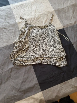 Leopardmönstrad linnetopp - Säljer en leopardmönstrad linnetopp med tunna axelband. Toppen är i ljusa toner med svart och beige mönster, har en lös passform och är perfekt för varma dagar. Materialet känns lätt och luftigt.