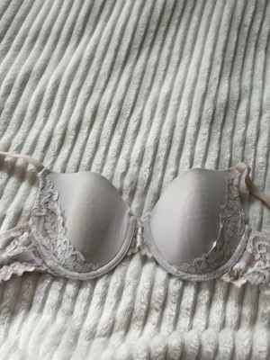 Ljusbeige push-up bh med spets - Säljer en ljusbeige push-up bh från Creem Luxury med vadderade kupor och fina spetsdetaljer längs kanterna. Bh:n har justerbara axelband och hakknäppning bak. Perfekt för dig som gillar en feminin och elegant stil. En liten fläck på den