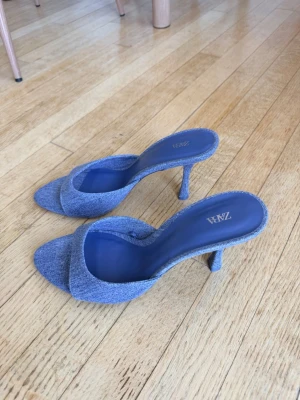 Blåa denim-pumps från Zara - Snygga blåa pumps från Zara i denimtyg med öppen tå och smal klack. Skorna har en modern och trendig design med bred rem över foten och bekväm innersula. Perfekta för att lyfta din outfit med en cool touch.