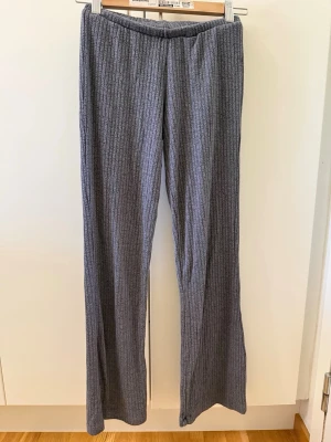 Grå ribbade mjukisbyxor - Mysiga grå mjukisbyxor med ribbad struktur och raka ben. Byxorna har resår i midjan för extra komfort och är tillverkade i ett mjukt, stretchigt material. Perfekta för chill dagar hemma eller när du vill vara bekväm men ändå se snygg ut.