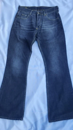 Blå bootcut jeans från Lee - Säljer ett par klassiska blå bootcut jeans från Lee med fem fickor och knappgylf. Jeansen har en snygg tvätt med ljusa slitningar och breda ben. Perfekta för dig som gillar en retrostil och vill ha ett par jeans med skön passform.