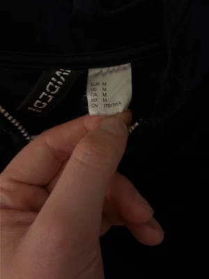 Svart hoodie i velour från H&M - Mjuk och stilren svart hoodie i velour från H&M . Tröjan har huva och breda muddar vid midjan och ärmsluten. Perfekt för en avslappnad och trendig look. Klassisk passform och skön känsla mot huden.