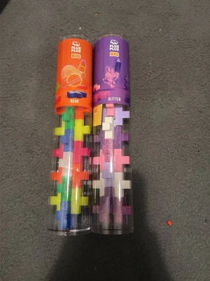 Plus Plus Big Neon & Glitter byggbitar - Två rör med Plus Plus Big byggbitar i olika färger, ett med neonfärger och ett med glitterfärger. Perfekt för kreativt byggande och lek. Bitarna är stora och kommer i färgglada nyanser som rosa, lila, grön, blå, vit och gul. 1 för 50 2 för 85