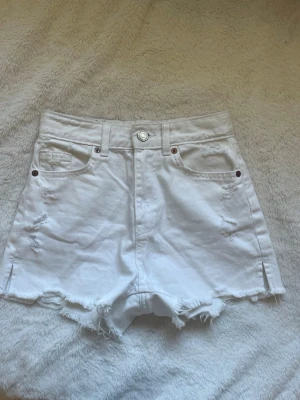Vita högmidjade jeansshorts - Säljer ett par vita högmidjade jeansshorts med råa kanter och slitna detaljer säljer shortsen för dom var för stora .
