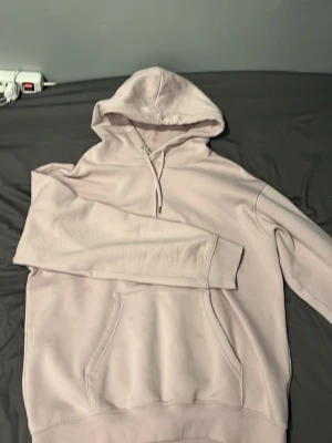 Ljusrosa hoodie H&M - En stilren ljusrosa hoodie med huva och dragsko. Hoodien har en klassisk magficka och ribbade muddar vid ärmslut och nederkant. Perfekt för en avslappnad look. Materialet känns mjukt och bekvämt, troligtvis bomullsblandning.